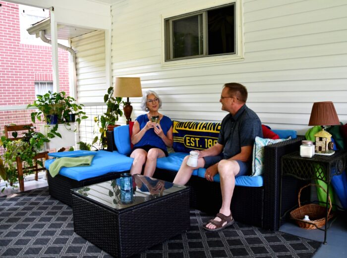 Man and woman sit on a couch on their screened-in back porch, enjoying their coffee.