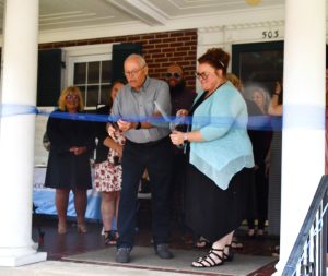 A man in a gray shirt and black pants and a woman in a blue top and black pants cut the ribbon to celebrate the opening of Seed Sower Manor. 