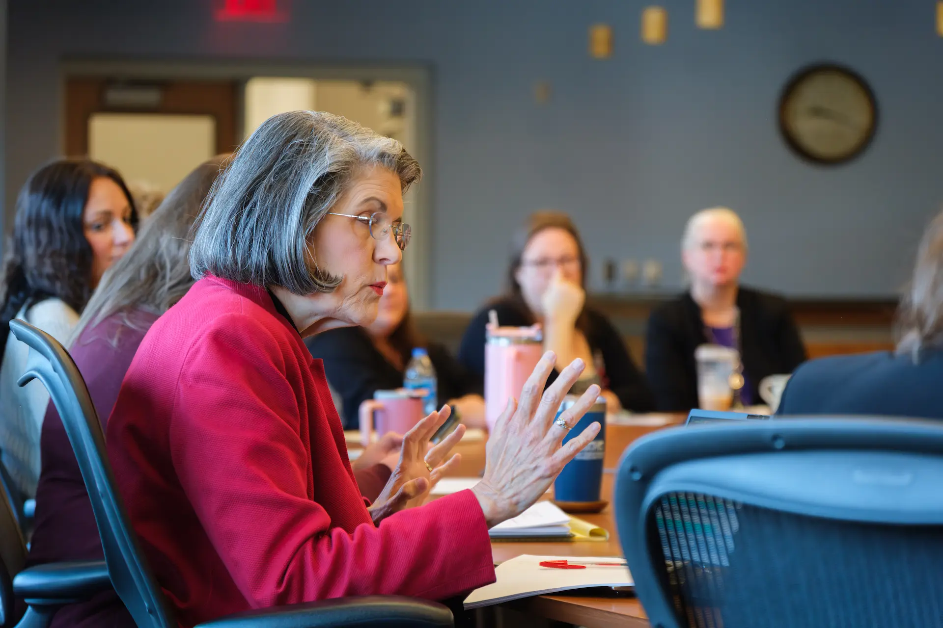 Person speaks and gestures during a meeting, reflecting engaged discussion in a professional setting.