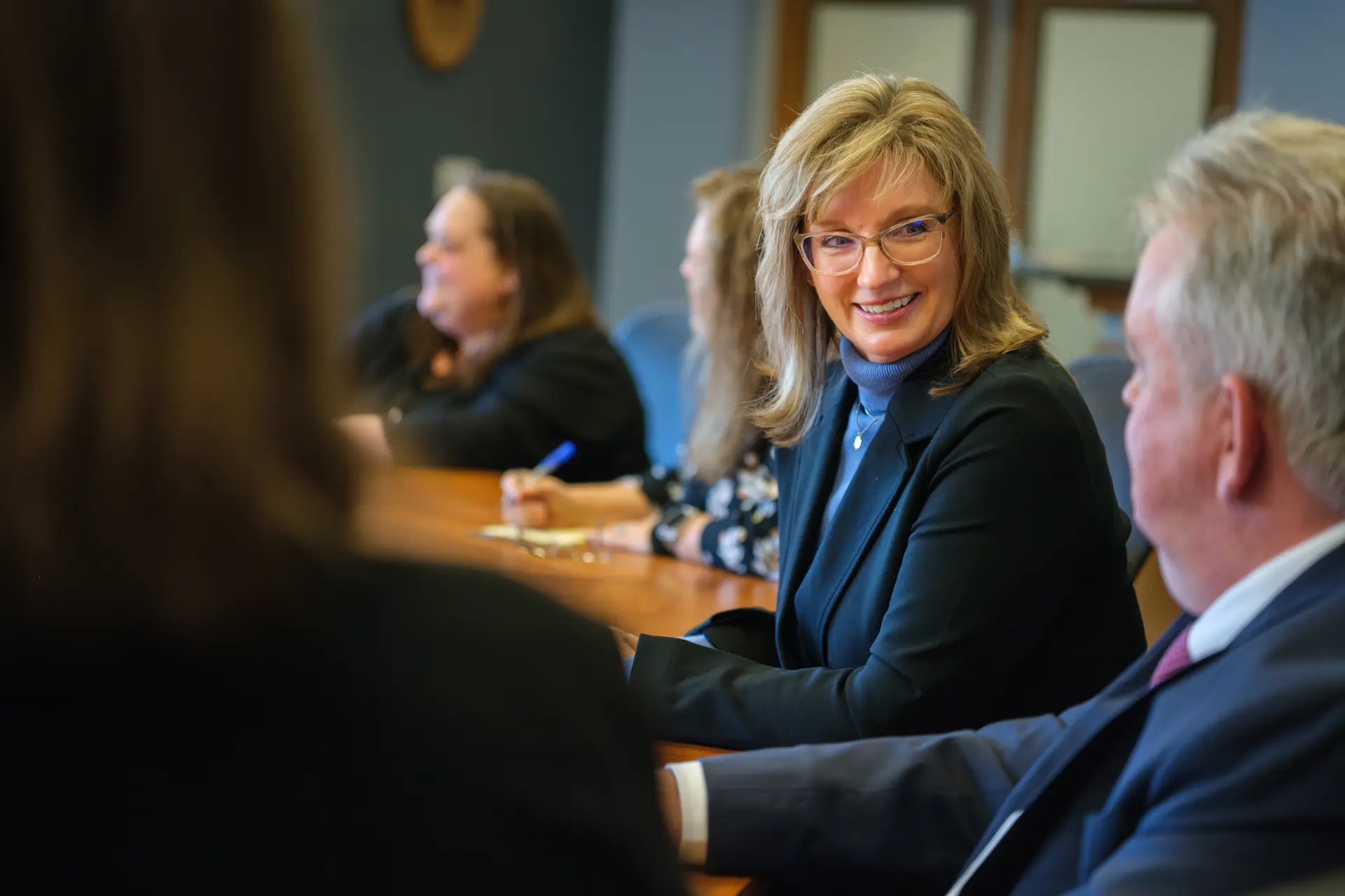 People meet at a conference table, sharing conversation in a collaborative and welcoming setting.