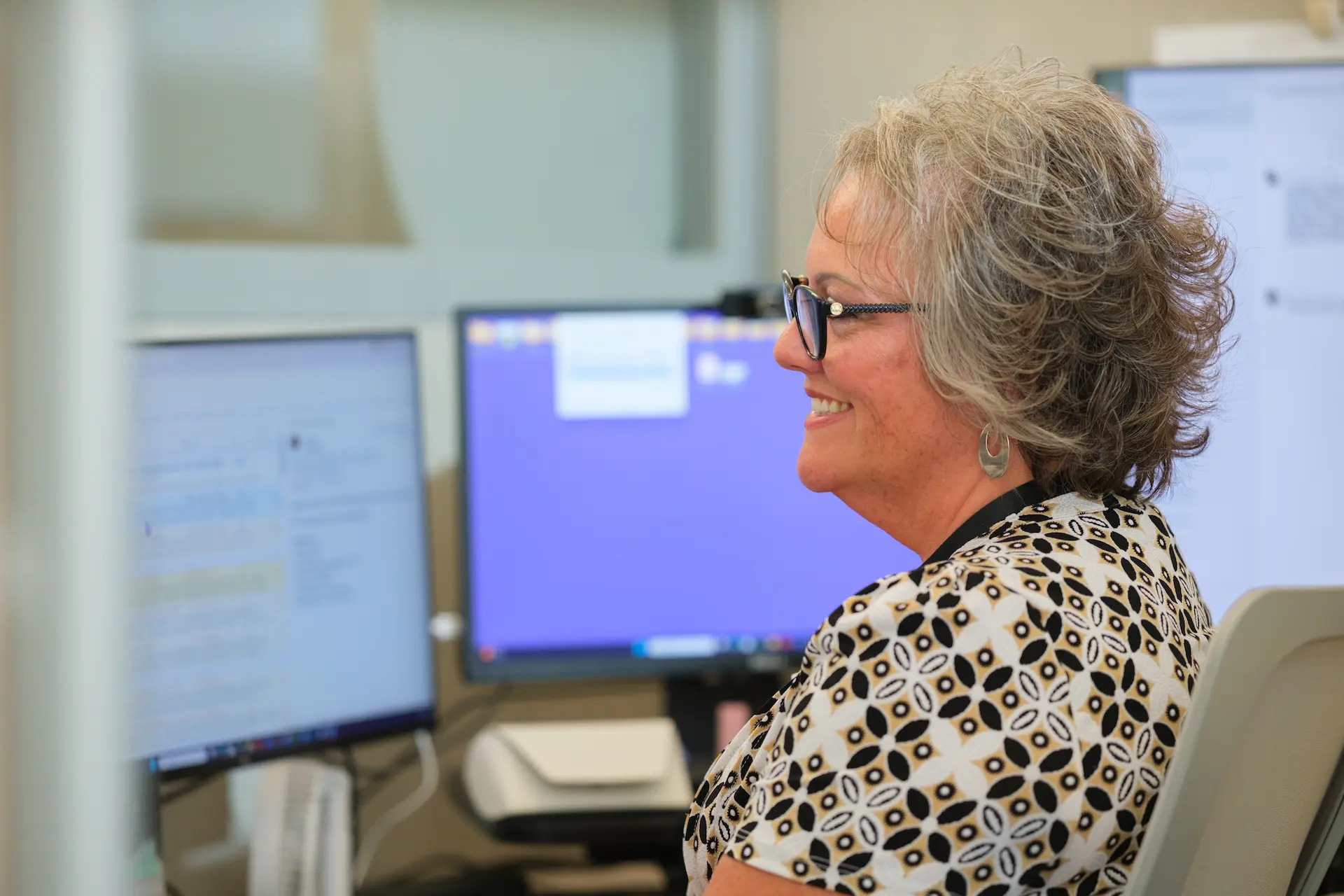 Person smiles at a workstation with dual monitors, reflecting a supportive and professional office environment.
