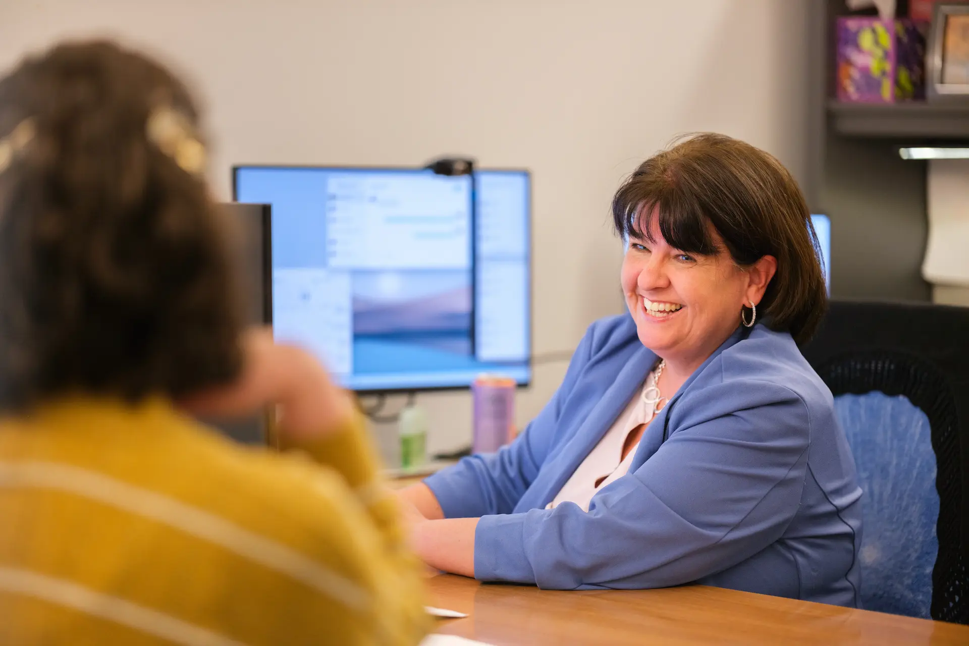 Person smiles while meeting with another individual in an office, reflecting a supportive and approachable environment.