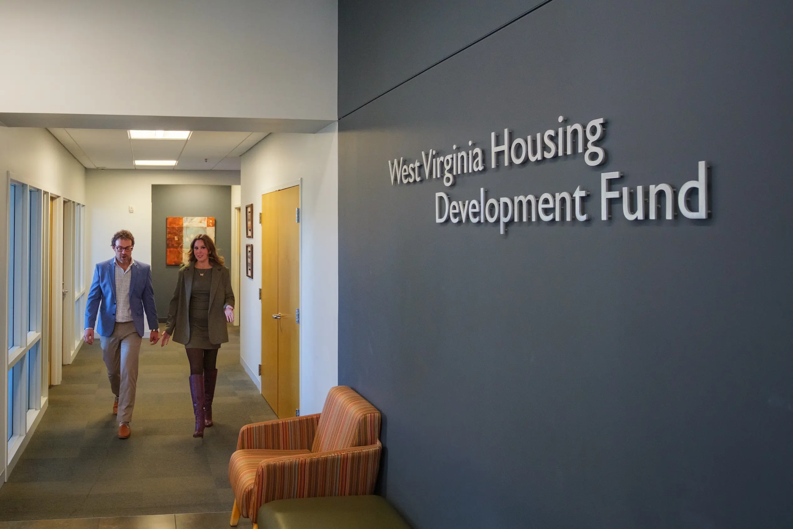 Two professionals walking down a hallway inside an office with a wall sign reading West Virginia Housing Development Fund