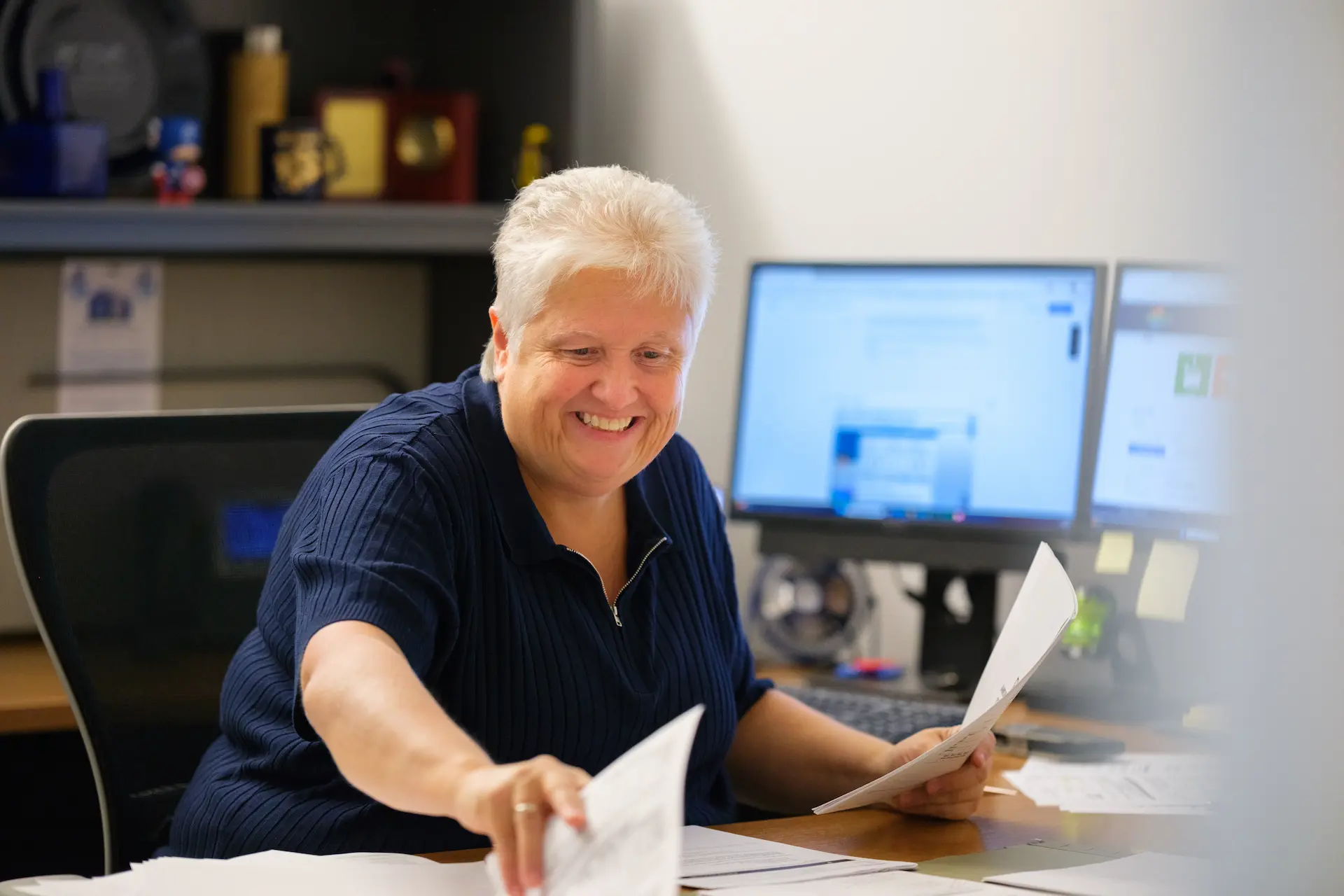 Person reviews paperwork at a desk in an office workspace.