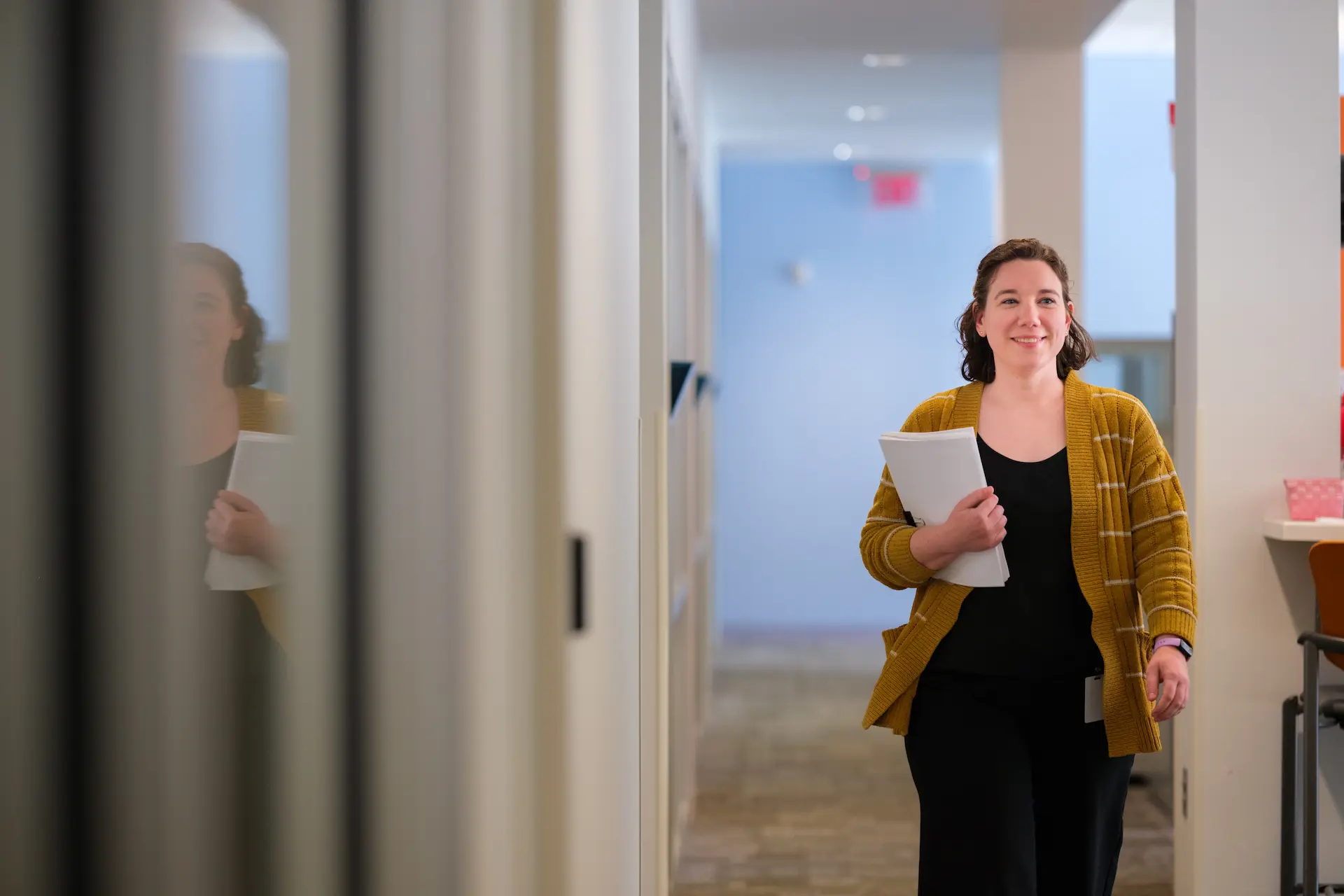 Person walks through an office hallway carrying documents.