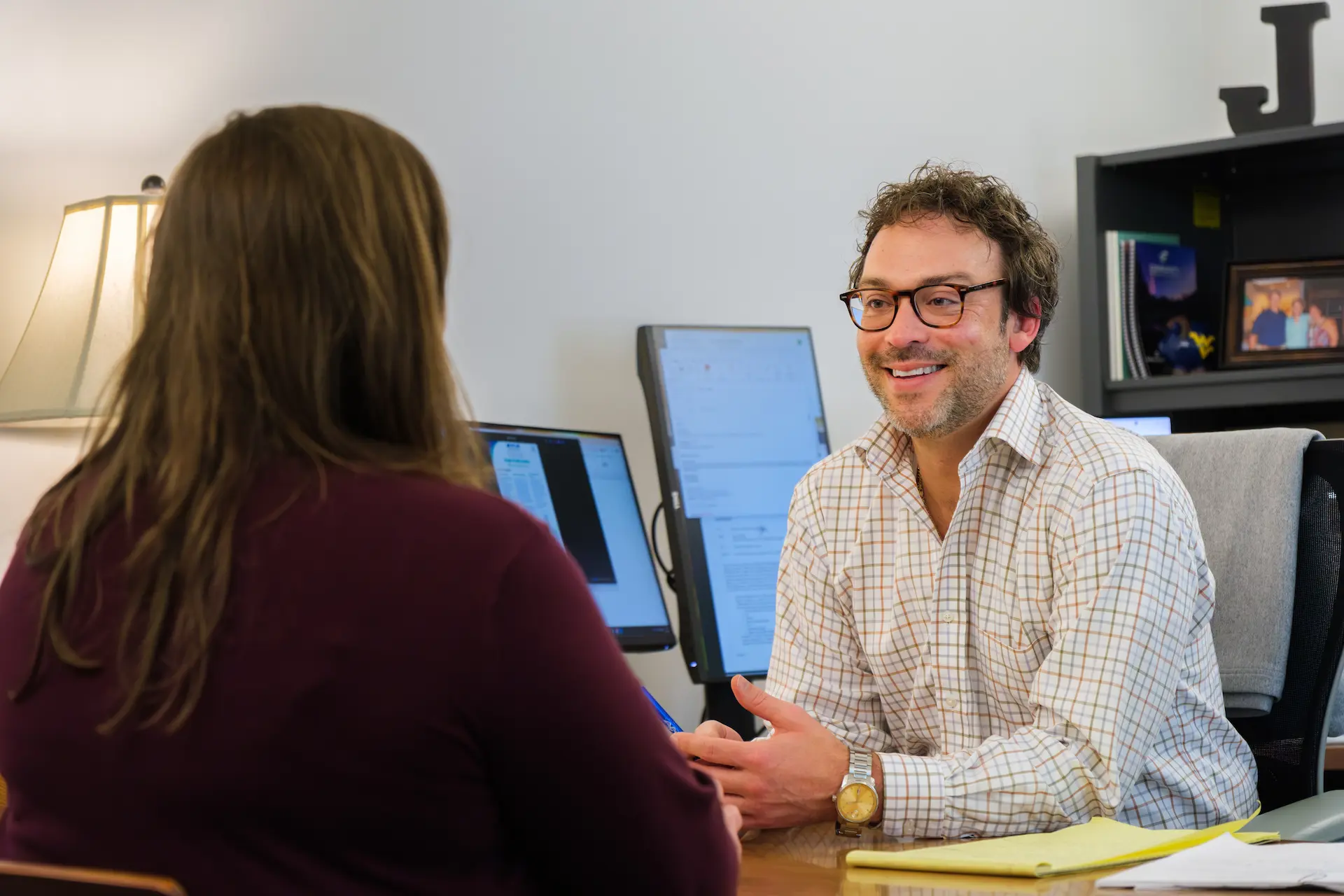 Two people meet at a desk, discussing information in an office setting.