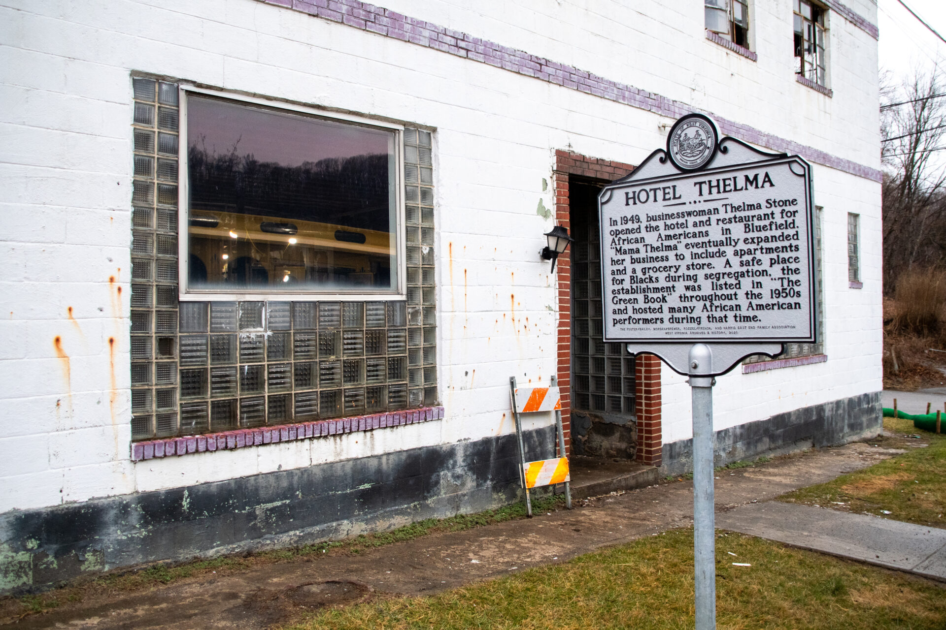 The exterior of Hotel Thelma, an aging structure built of white cinder block. A marker stands in front of the building, noting the hotel's recognition in the Green Book, a guidebook for Black travelers during the Jim Crow era.