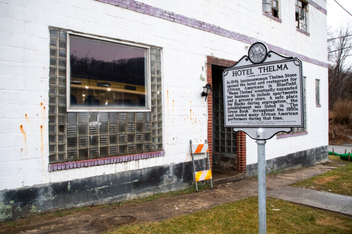 The exterior of Hotel Thelma, an aging structure built of white cinder block. A marker stands in front of the building, noting the hotel's recognition in the Green Book, a guidebook for Black travelers during the Jim Crow era.