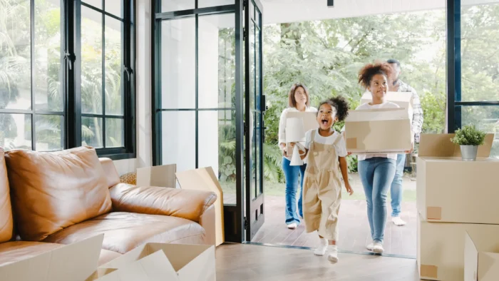 An excited family carrying cardboard moving boxes into their bright new home.