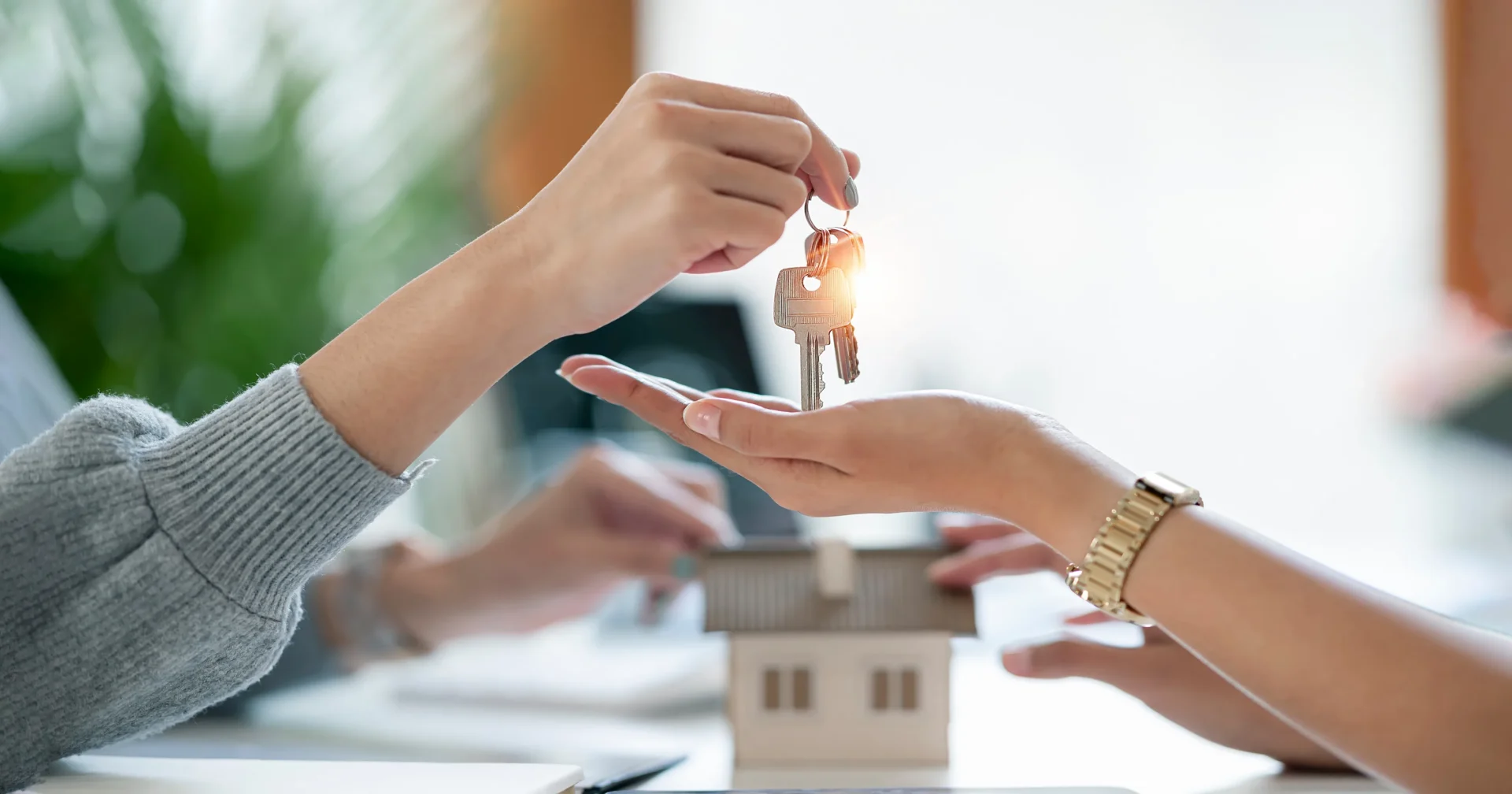 Close-up of a hand passing house keys to another person above a small model house.