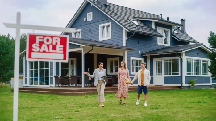 Real estate agent showing a couple a newly listed home with a for sale sign in the foreground.